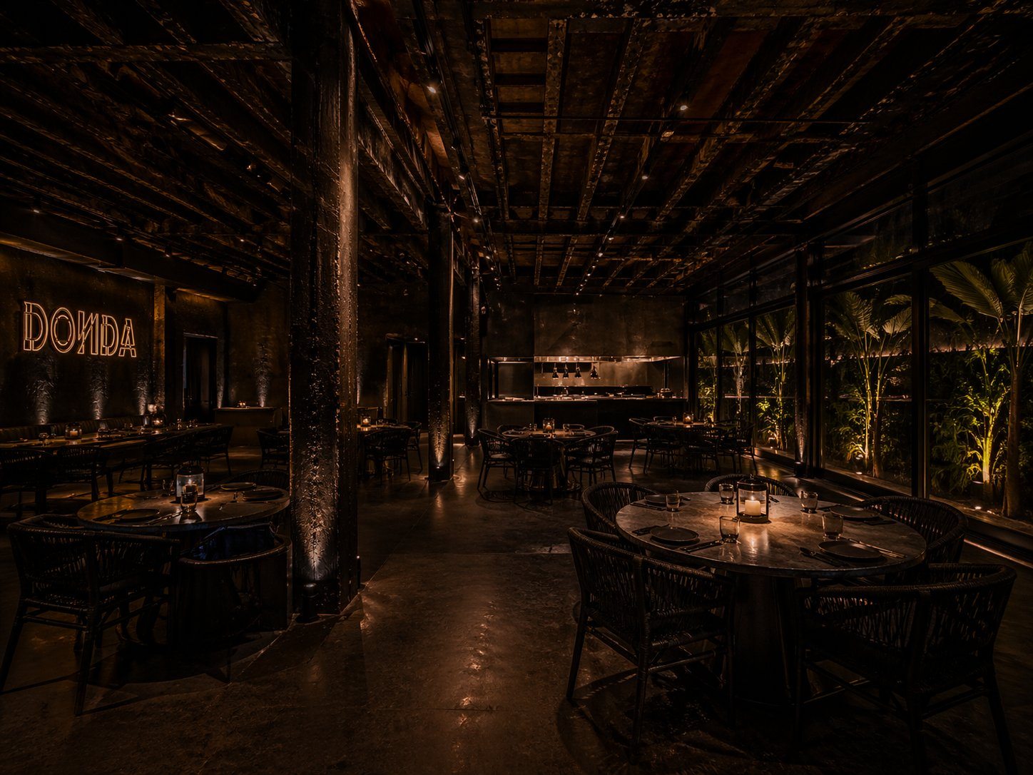 The DONDE dining room at night: candlelit tables, the DONDE neon glowing on the far wall, the open kitchen behind and the planted terrace alongside